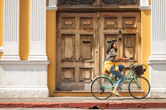 Young woman on a bicycle. Beautiful Hispanic teen riding a bike in front of a colonial house.