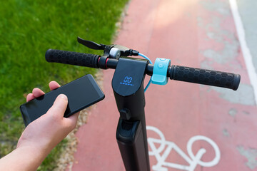 The phone in the hand of a man using an ecological transport scooter on a bicycle road in the park. Modern urban lifestyle - 526785824