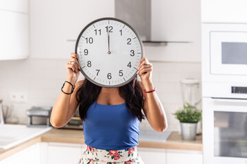 Woman holds a clock showing one minute to twelve in fron of her face