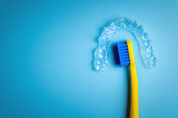 An invisible plastic aligner for correcting teeth to straighten teeth lies on a blue background with a toothbrush