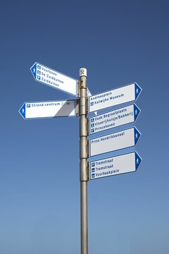 Vertical shot of a post with different signs against a blue sky in Katwijk, Netherlands