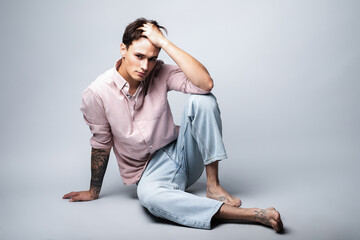 Male portrait on a gray background. A young guy in blue jeans and a shirt on a gray background. Model looking guy