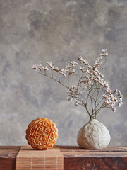 front view of moon cake on bamboo mat and vase with dried flowers branches on wood. Mid-autumn festival composition, copy space.