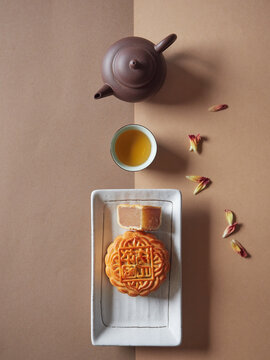 Moon Cake on a plate and a quarter cut showing the stuffing, tea served in cup and teapot. Traditional chinese cake for Mid Autumn Festival. Top view.