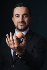 Close-up of an egg in the hand of a modern man in a fashionable suit, a man in a black suit is holding an egg