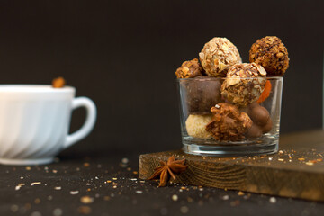 Glass with truffle sweets on a black background. White cup of coffee. Sweet food. Festive dessert.