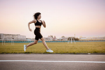 curly woman runner, runs around the stadium in sportswear. Morning running.