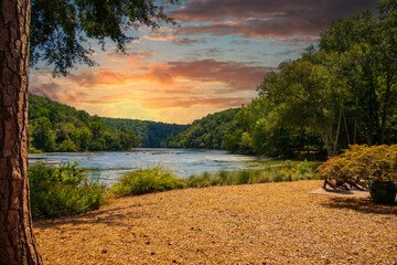 a gorgeous summer landscape along the Chattahoochee river with flowing river water surrounded by lush green trees, grass and plants with powerful clouds at sunset at Walton On The Chattahoochee - obrazy, fototapety, plakaty