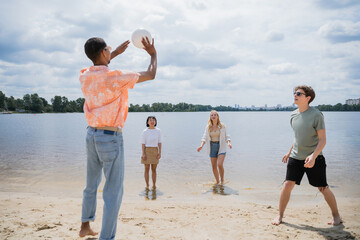 african american man passing ball while playing beach volleyball with multiethnic friends.
