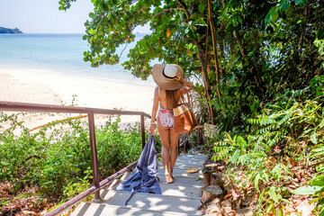 Back view of travel woman walking on stairs on the way to empty sandy beach