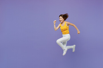 Full body side view happy smiling surprised young woman 20s she wearing yellow tank shirt jump high run fast isolated on plain pastel light purple background studio portrait. People lifestyle concept.