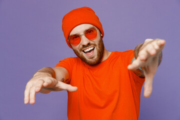 Young happy cool fun european man 20s wear red hat t-shirt sunglasses stretch hands to camera dance...