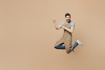 Fototapeta na wymiar Full body young man barista barman employee in brown apron work in coffee shop jump high point finger aside on workspace isolated on plain pastel light beige background Small business startup concept.