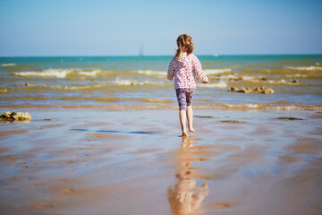 Preschooler girl playing on the sand beach at Atlantic coast of Normandy, France - obrazy, fototapety, plakaty