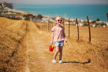 Preschooler girl going to beach at Atlantic coast of Normandy, France. Outdoor summer activities for kids - obrazy, fototapety, plakaty