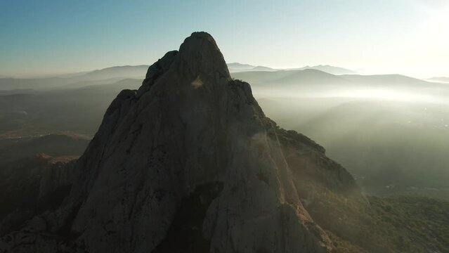 Aerial view of Pena de Bernal mountain with foggy rocky hills on the horizon in Mexico