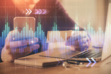 Double exposure of man's hands holding and using a phone and financial graph drawing. Analysis concept.