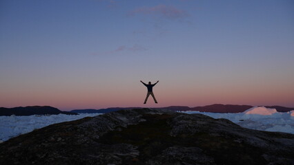 Person silhouette jumping in the air with icebergs in the back in Greenland