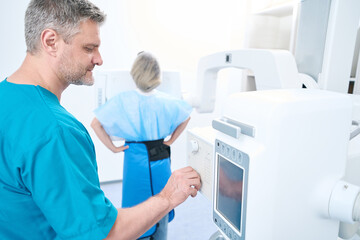 Focused adult doctor adjusts the buttons of the x-ray machine