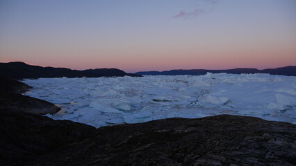 View from cliff overlooking bay of icebergs in Greenland at night