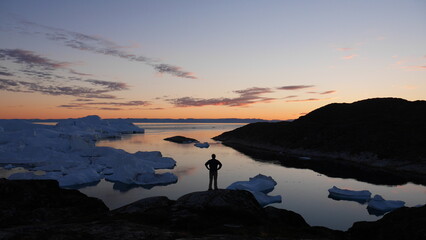 Person standing on cliff overlooking bay of icebergs in Greenland