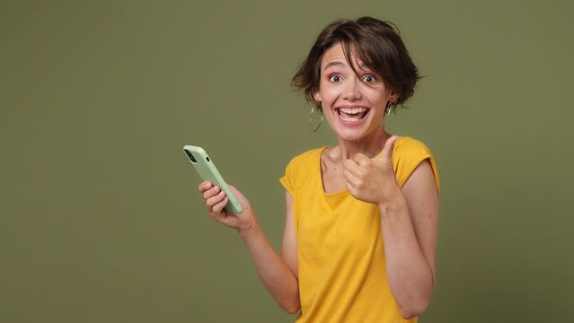 Side view young woman wear yellow t-shirt hold use mobile cell phone type swipe chatting send sms doing online shopping order delivery to home isolated on plain pastel green background studio portrait