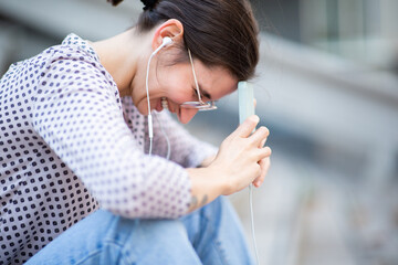 Smiling woman enjoying listening to music with mobile phone and earphones outside
