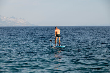 Man standing and rowing on his paddle board across the Mimice beach bay, Croatia