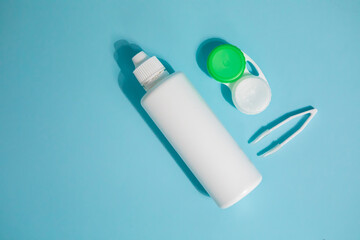 Packages with contact lenses, case, tweezers and drops on blue background