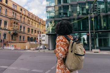 back view of curly young woman with backpack standing on urban street in berlin.