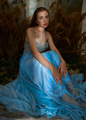 an elegant woman in a long blue dress is sitting in a fabulous location