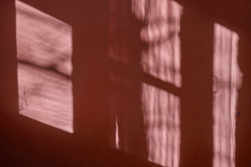 a dark red wall with beautiful sun light and window frame shadow shine on. Background. Morning sunlight shine through  the window  on dark green wall inside the room.