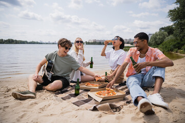 happy multicultural friends having beach picnic with beer and pizza.