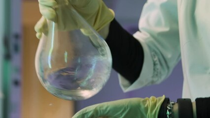 Laboratory researcher experimenting with liquid substance inside flask. Stock footage. Close up of mixing chemical solution.