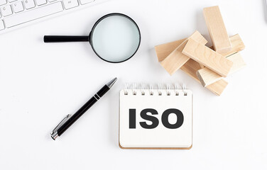 ISO word written on notebook with block magnifier and pen , business concept.