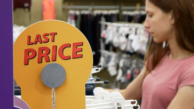 A sign LAST PRICE in a clothing store and a woman choosing the clothes behind it
