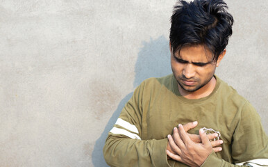 concept of chest pain heart attack. Young indian man putting his both hand on chest suffering from...