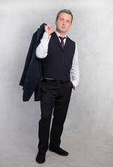 Vertical photo of a man in a vest holding a jacket in his hand.