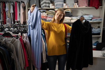 happy young woman choosing between two sweatshirts in mall or clothing store. sale, clothing,...
