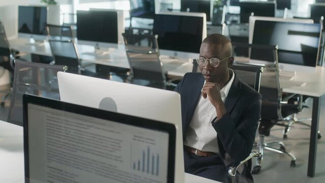 African-american attractive businessman in suit working on laptop in office, happy black ceo looking at computer screen thinks and analyzes looking at the computer screen, browsing web, using software