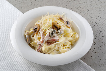 Spaghetti with ham and champignon mushrooms sprinkled with cheese. On a white plate, black background. copyspace.