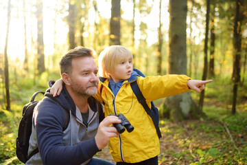School child and his father hiking together and exploring nature with binoculars at autumn. Little boy and his dad spend quality family time in sunny forest of second summer. Father's Day.