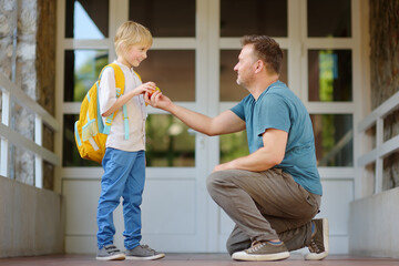 Little schoolboy with his father goes to school after summer holiday. Parent accompanies or meets...