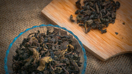 Selective focus Dried roasted green tea leaves on the bowl on burlap background, Japanese tea,...