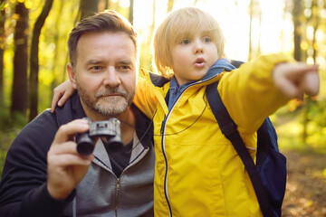 School child and his father hiking together and exploring nature with binoculars at autumn. Little...