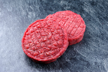 Rohes Barbecue Rindfleisch Hamburger Patty angeboten als close-up auf grauen Hintergrund mit Textfreiraum
