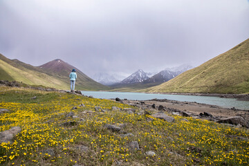 A lone hiker looks over lake Kol Akok and the high peaks of the Tian Shan mountain range of...
