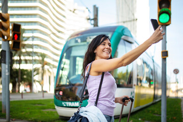 Happy woman taking selfie in front of city tram