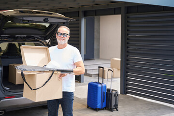 Fototapeta na wymiar Smiling man moving boxes from car into new house