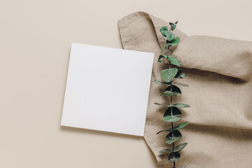 Blank paper card on linen cloth and eucalyptus leaves. Top view, flat lay. Minimal aesthetic card...